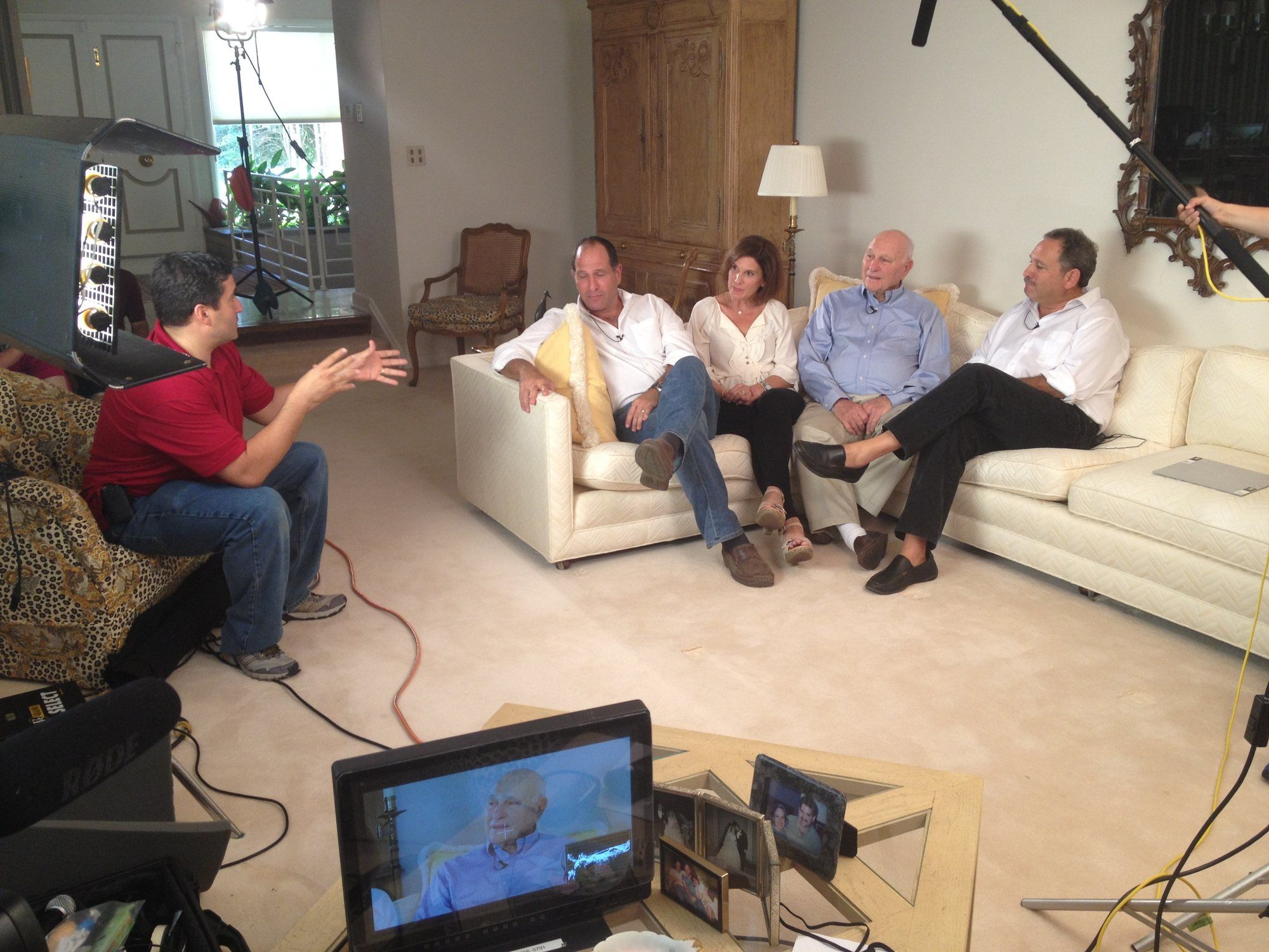 Filming an interview with one of the key program sponsors in their home: three guests on a sofa, the interviewer and a camera monitor in the foreground.