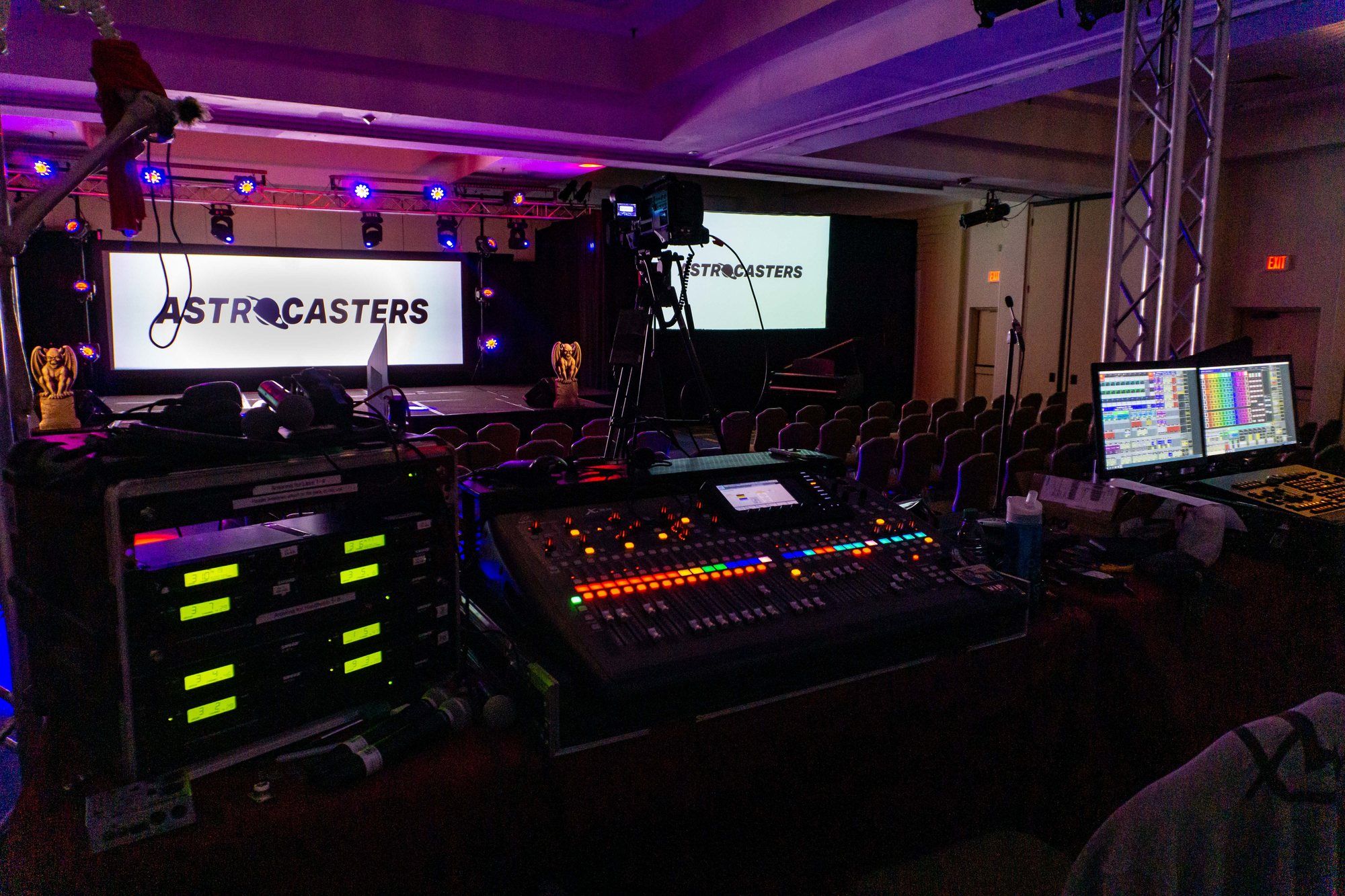 A front-of-house position with an audio console, in front of a stage with Astrocasters projection screens.