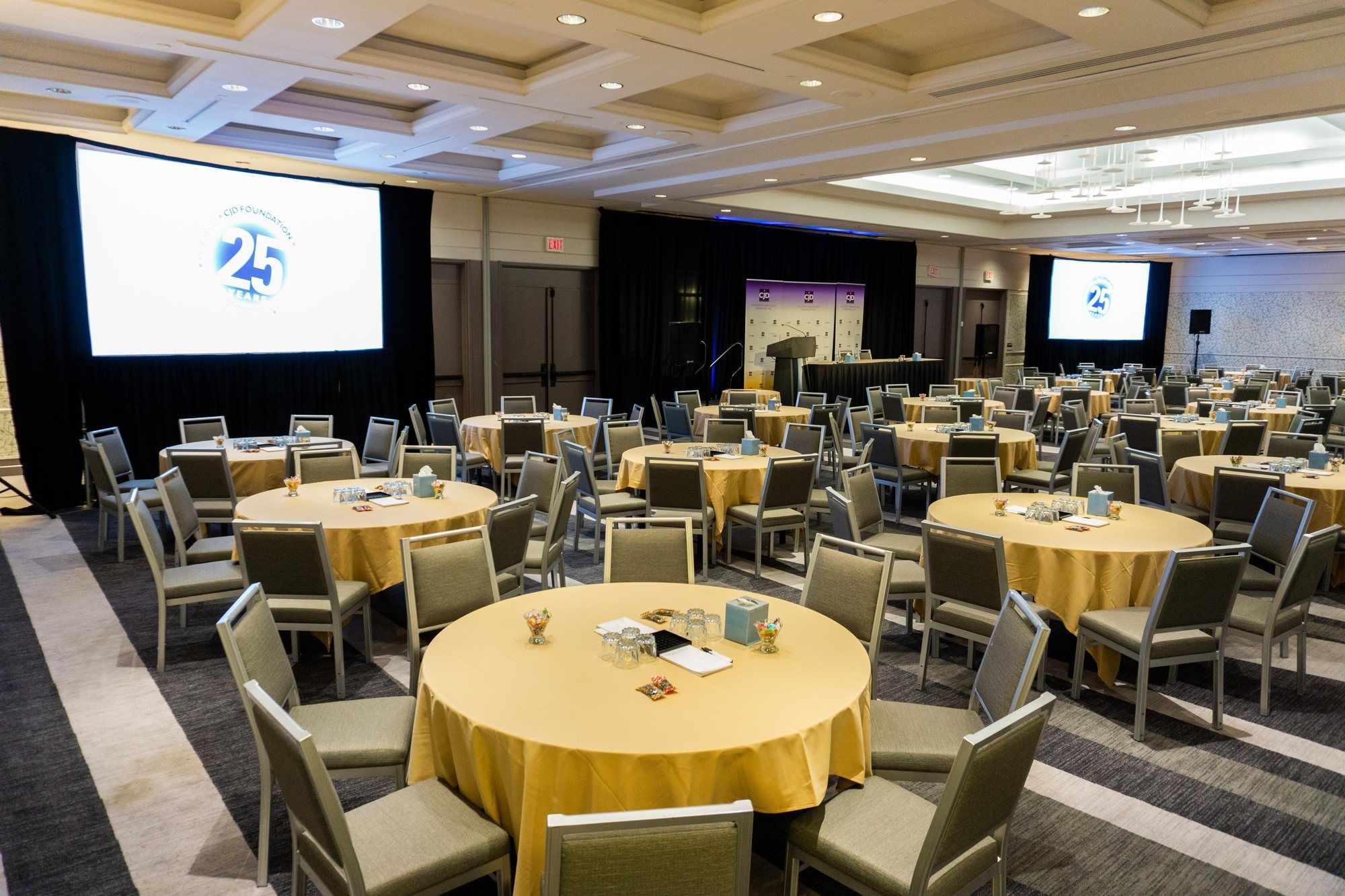 A hotel ballroom set with round tables, with projection screens at the front and side.