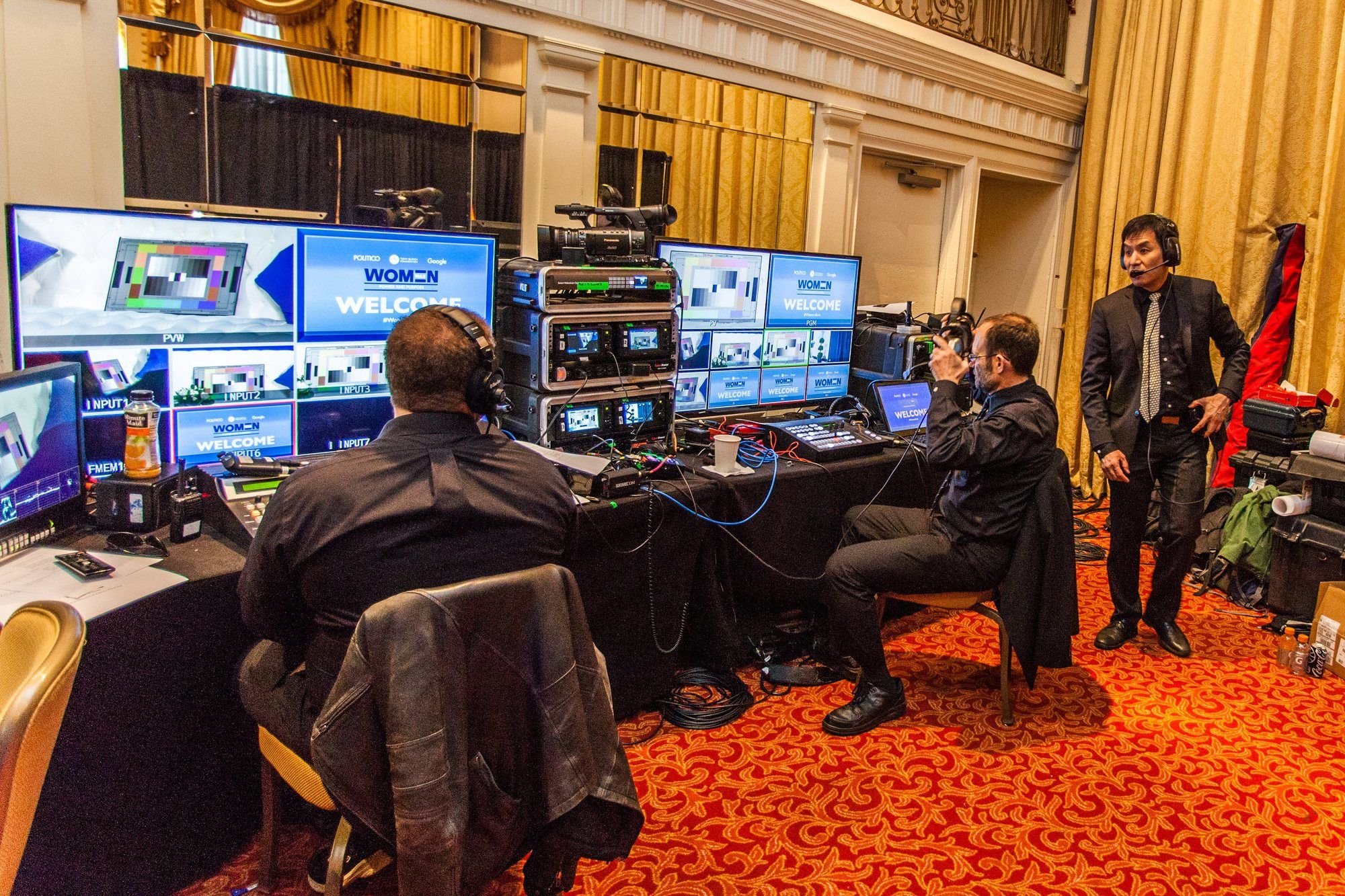 Astrocasters crew at a video control position in a gala ballroom, with switchers and a row of monitors.