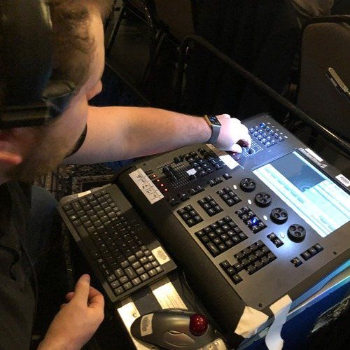 A technician's hands on a lighting console during a show.